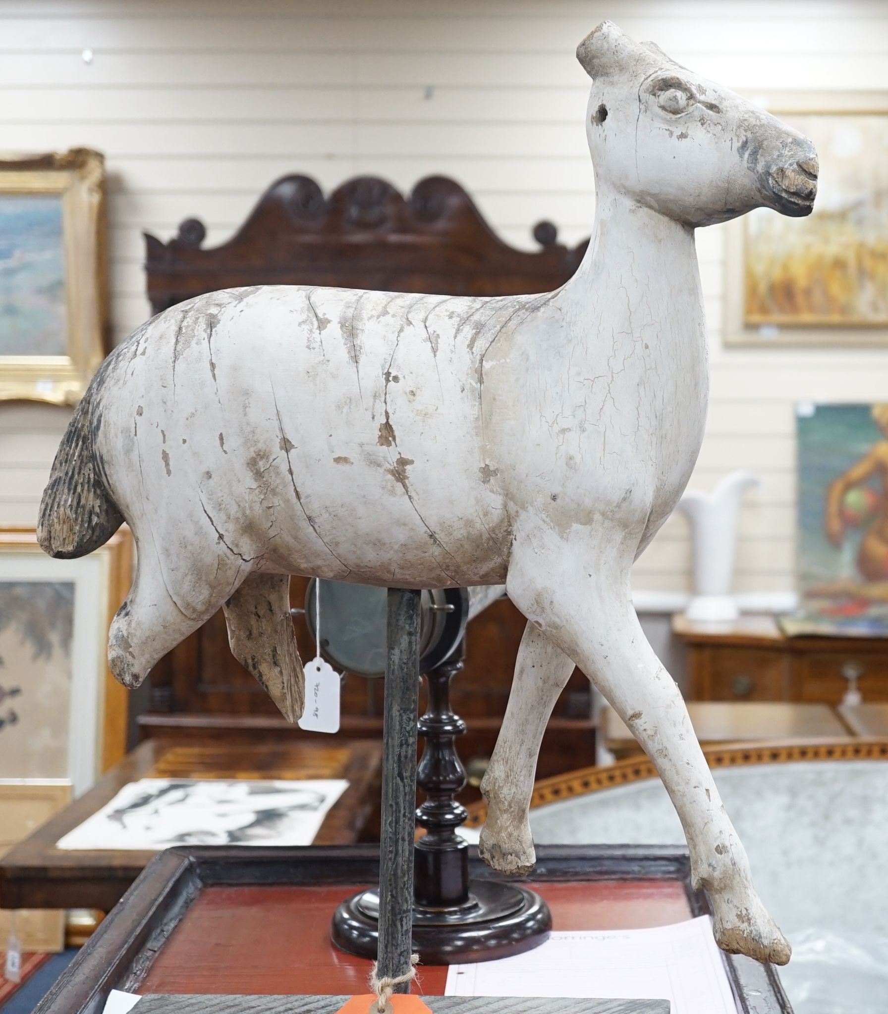 A carved and painted wood model of a goat, with distressed paint, on stand. 66cm